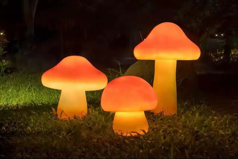Three illuminated mushrooms of different heights glowing warm orange on a lawn at night